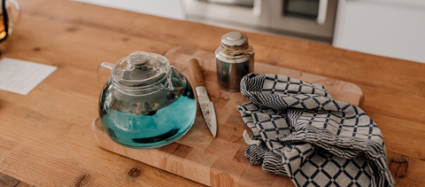 Blauwe thee in glazen theepot op houten plank